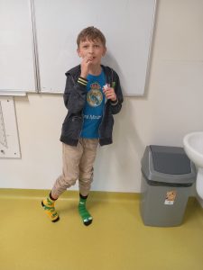 Uczeń klasy piątej je czekoladki stojąc przy tablicy w skarpetkach na nogach, które otrzymał w prezencie od koleżanek.