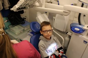 Uczeń klasy piątej siedzi na fotelu dentystycznym w dentobusie. Chłopiec patrzy wprost w stronę aparatu.