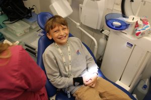 Uczeń klasy piątej siedzi na fotelu dentystycznym w dentobusie i szeroko się uśmiecha.