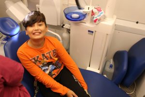 Uczeń klasy piątej siedzi na fotelu dentystycznym w dentobusie i szeroko się uśmiecha.
