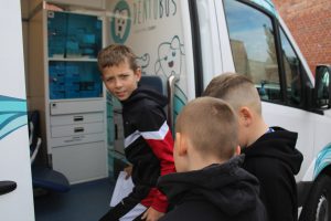 Trzech uczniów wchodzi o dentobusa. Jeden z nich stojący najwyżej odwraca się przodem do aparatu.