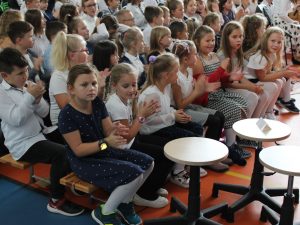 Zdjęcie klaszczącej widowni. W prawym rogu widoczne trzy puste, obrotowe krzesła.