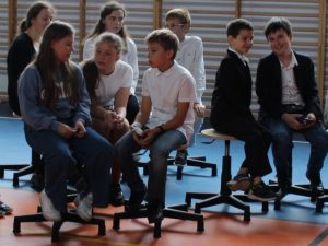 Trzy grupki uczniów siedzą na obrotowych krzesłach i rozmawiają między sobą.