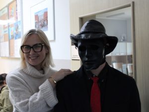 Nauczycielka pozuje do wspólnego zdjęcia z uczniem z czarna maska i kapeluszem na głowie. Nauczycielka opiera dłonie o ramię ucznia i szeroko się usmiecha.
