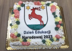Zdjęcie tortu wykonanego z okazji Dnia Edukacji narodowej. Na białym tle ozdobionym kolorowymi kwiatami logo gminy Łysomice a pod spodem napis : "Dzień Edukacji Narodowej 2023".