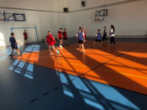 Uczniowie stoją w różnych odstępach od siebie na sali gimnastycznej. Zdjęcie wykonane w oddali.