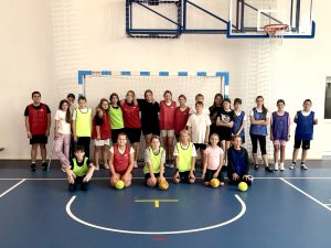 Uczniowie klasy szóstej pozują do wspólnego zdjęcia stojąc w świetle bramki na sali gimnastycznej. Uczniowie w pierwszym rzędzie klęczą na kolanach a przy nich leżą piłki.