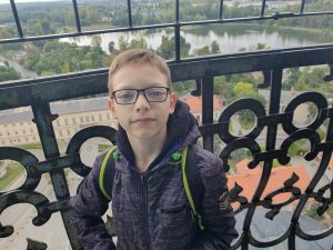 Chłopiec pozuje do zdjęcia na punkcie widokowym. Za nim widać zdobioną balustradę oraz płynąca przez Gniezno rzekę.