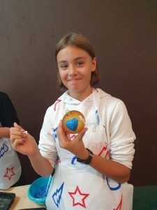 Uczennica pozuje do zdjęcia z trzymaną w dłoni bombką. Na bombce widać serduszko w kolorze morskim.