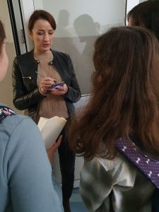 Nauczycielka wypełnia karteczkę z zadaniami z tabliczki mnożenia. Przed nią stoją uczniowie.