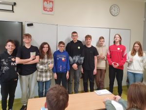 Uczniowie klasy ósmej pozują do wspólnego zdjęcia z naklejonymi na ubraniu odznaki "Mistrza Tabliczki Mnożenia".