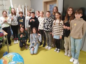 Uczniowie klasy szóstej pozują do wspólnego zdjęcia trzymając w dłoniach lub mając naklejone na ubraniu odznaki "Mistrza Tabliczki Mnożenia".