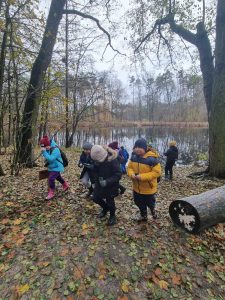 Uczniowie idą przez las. W tle widać staw.