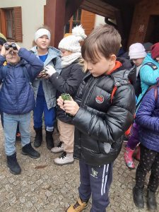 Dzieci stoją przed budynkiem szkoły leśnej na Barbarce. Oglądają otrzymane lornetki.