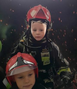 Uczeń pozuje do zdjęcia stojąc za ścianka z wyciętym otworem na głowę. Przed nim stoi jego kolega.