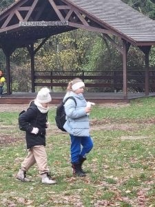 Dwie uczennice idą przez polanę. W tle widać drewnianą altanę.