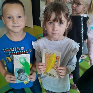 Dwoje uczniów stoi na dywanie. Dzieci w dłoniach trzymają swoje pamiątki z muzeum druku i piśmiennictwa.