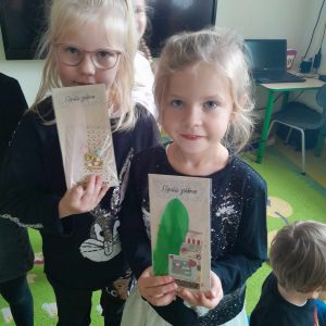 Dwie uczennice stoją na dywanie. Dziewczynki trzymają w dłoniach trzymają swoje pamiątki z muzeum druku i piśmiennictwa.