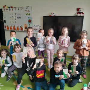 Uczniowie oddziału przedszkolnego pozują do wspólnego zdjęcia na dywanie. Dzieci trzymają przed sobą otrzymane w muzeum piśmiennictwa pamiątki.