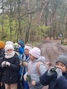 Uczniowie stoją na leśnej ścieżki. Dzieci wyposażone są w zielone lornetki.