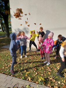 Uczniowie klasy drugiej stoją na szczycie budynku szkoły i podrzucają w górę liście.