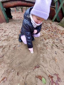 Uczennica pochyla się nad piaskiem na którym odciska tropy zwierząt przy pomocy gipsowego odlewu.