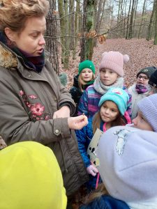Uczniowie stoją zgromadzeni wokół Pani, która w dłoniach trzyma małego robaka.