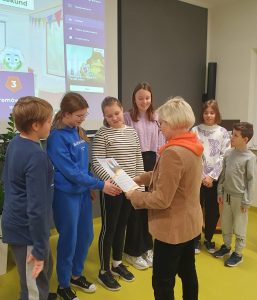 Pani Dyrektor wręcza dyplom jednej z drużyn znajdujących się na podium konkursu. Dzieci stoją w rzędzie.