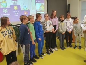 Uczniowie którzy zajęli pierwsze trzy miejsca w konkursie stoją w jednym rzędzie obok siebie. Jedna z dziewczynek trzyma otrzymany dyplom.