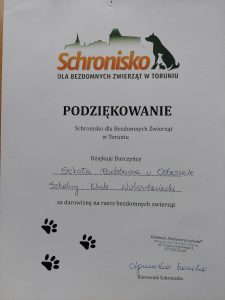 Zdjęcie podziękowań od schroniska dla Szkoły za dostarczoną karmę. Na białym tle u góry grafika psa z zarysem miasta Torunia i napis : "SCHRONISKO DLA BEZDOMNYCH ZWIERZĄT W TORUNIU". Poniżej : "PODZIEKOWANIE Schronisko dla Bezdomnych Zwierząt w Toruniu Dziękuje Darczyńcy Szkoła Podstawowa w Ostaszewie Szkolny Klub Wolontariacki za darowiznę na rzecz bezdomnych zwierząt". Poniżej trzy grafiki przedstawiające odciski psich łapek oraz pieczątka i podpis kierownika schroniska.