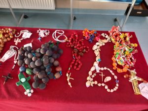 Zdjęcie rozłożonych na stole przykrytym czerwonym materiałem różańców zgłoszonych do konkursu.