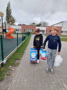 Dwóch uczniów idzie szkolnym boiskiem niosąc torby z karmą dla zwierząt.