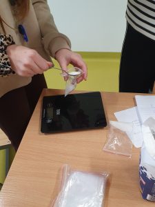 Uczennica odmierza cukier przy pomocy łyżeczki do strunowego woreczka. Obok niej na stole leży waga kuchenna.