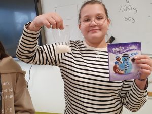 Uczennica klasy szóstej trzyma w jednej dłoni woreczek z cukrem a w drugiej opakowanie po słodkiej przekąsce.