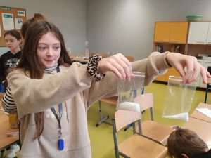 Uczennica klasy szóstej trzyma w wyciągniętych w bok dłoniach dwa woreczki strunowe z cukrem.