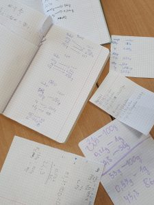 Zdjęcie rozłożonych na stole zeszytów i kartek, na których uczniowie dokonywali przeliczenia zawartości cukru.