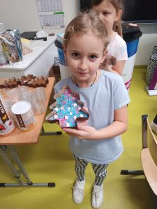 Uczennica klasy pierwszej pokazuje przygotowaną przez siebie czekoladę w foremce w kształcie choinki.