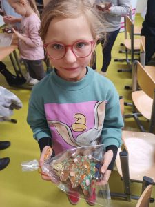 Uczennica klasy pierwszej pokazuje przygotowaną przez siebie czekoladę w foremce w kształcie choinki. Czekolada zapakowana jest w przezroczystą folię.