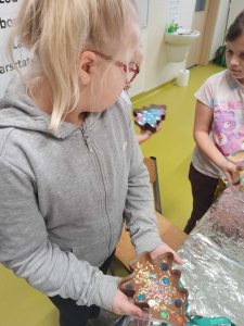 Uczennica klasy pierwszej trzyma w dłoni przygotowaną przez siebie czekoladę. Czekolada umieszczona jest w formie w kształcie choinki.