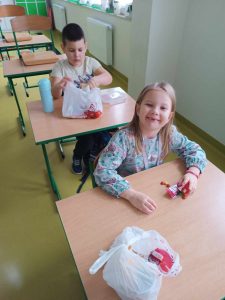 Dwoje uczniów siedzi przy stolikach, na których położone są siatki z mikołajkowymi upominkami. Dzieci je oglądają.