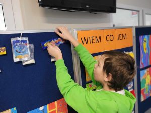 Uczeń przyczepia do granatowej tablicy opakowanie po wafelku wraz z torebką z cukrem pokazującą wartość cukru w tym produkcie.