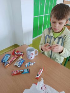 Uczeń siedzi przy stoliku, na którym rozłożone są słodkie upominki od Mikołaja oraz kubek.