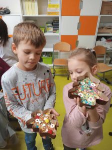 Dwoje uczniów klasy pierwszej pokazuje przygotowane przez siebie czekolady w foremkach w kształcie choinek.