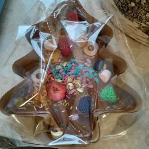 Zdjęcie wykonanej i zapakowanej w przezroczystą folię czekolady w kształcie choinki umieszczonej w papierowej foremce.