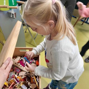 Uczennica oddziału przedszkolnego pochyla się nad drewnianą skrzyneczką, w której umieszczone są drobne prezenty dla dzieci za dobrze rozwiązane zadania.