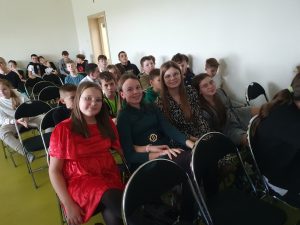 Cztery uczennice klasy szóstej pozują do wspólnego zdjęcia siedząc na krzesełkach w sali teatralnej. Za nimi widać innych uczniów.