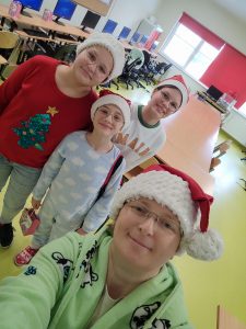 Nauczycielka w szlafroku i czapeczce Mikołaja robi zdjęcie sobie i stojących za nią trzech uczennicom ubranych w piżamy.