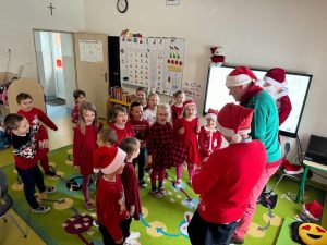 Uczniowie oddziału przedszkolnego stoją przed Radnym z gminy, świętym Mikołajem oraz Panią Dyrektor. Dzieci się uśmiechają.