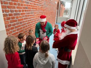Radny z gminy w asyście świętego Mikołaja rozdaje dzieciom na szkolnym korytarzu czekolady.