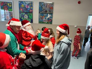 Radny z gminy w asyście świętego Mikołaja rozdaje dzieciom na szkolnym korytarzu czekolady.